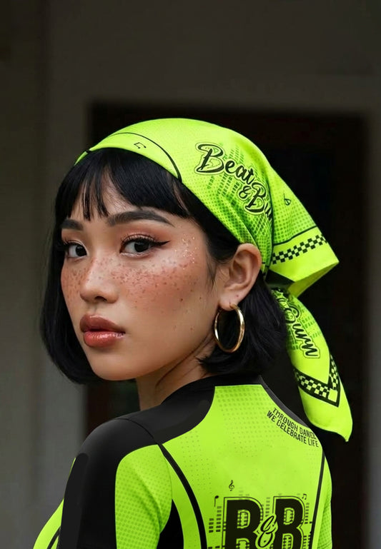 A woman with short black hair and freckles wears a bright neon yellow-green bandana headscarf with black text reading 'Beat & Burn.