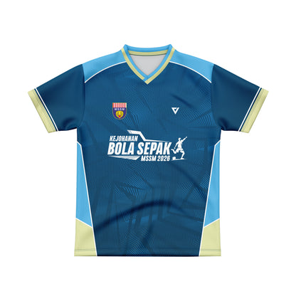A blue and light blue short-sleeve sports jersey with cream accents, featuring a V-neck, a crest on the left chest, a white stylized logo on the right chest, and a central white graphic reading 'KEJOHANAN BOLA SEPAK MSSM 2026'.